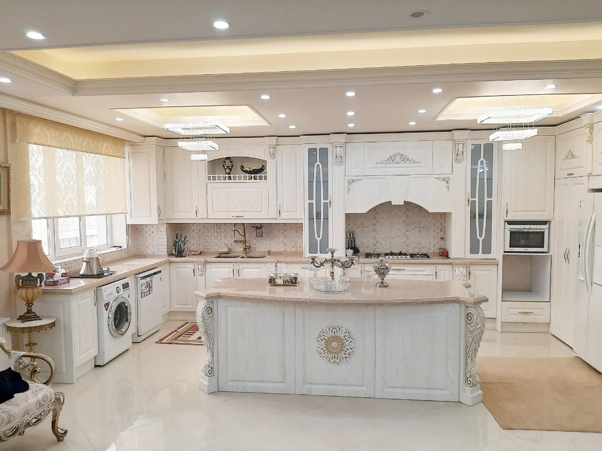 کابینت و جزیره کلاسیک سفید ممبران با منبت‌کاری‌های طلایی همراه با درب ویترینی