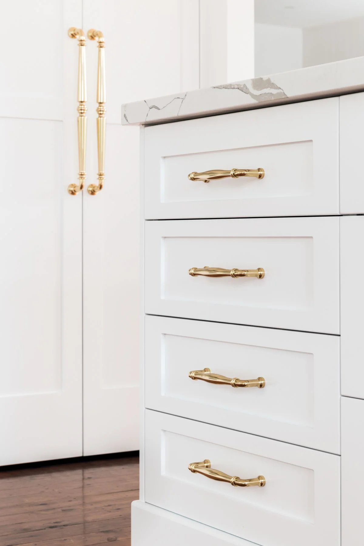 دستگیره کابینت کلاسیک طلایی براق با جزئیات در مرکز دستگیره و کابینت سفید نئوکلاسیک