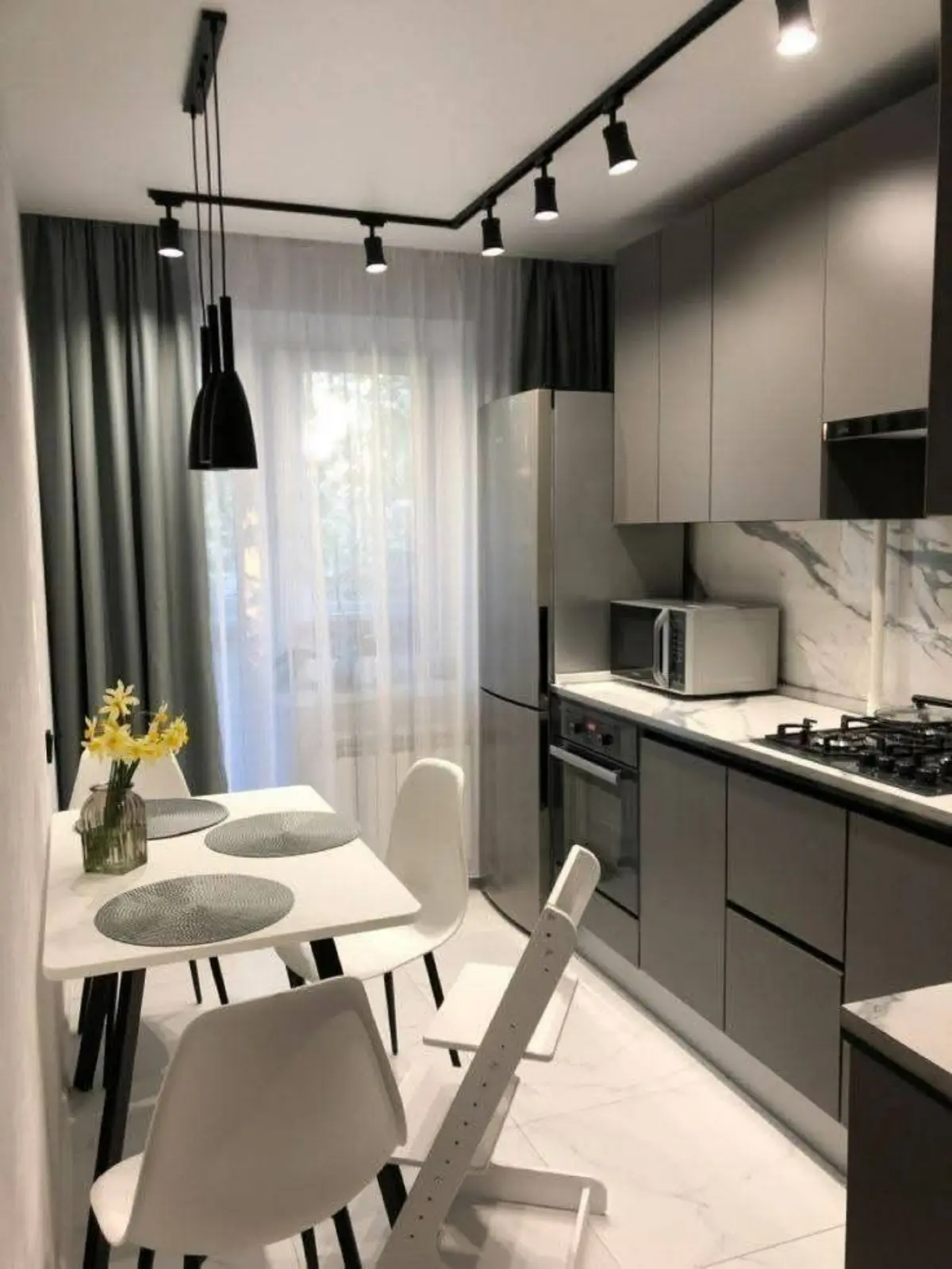 کابینت سفید طوسی مدرن با میز ناهارخوری سفید و پرده سفید طوسی و چراغ‌های مشکی
