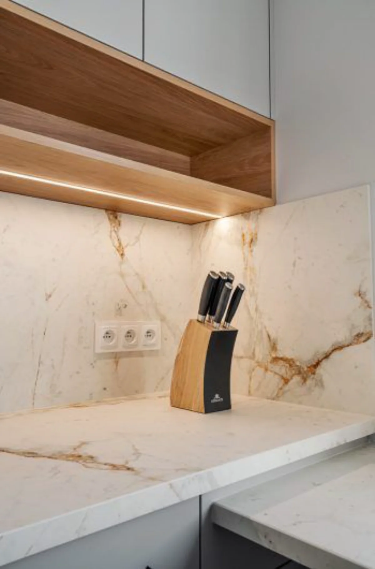 صفحه کابینت 3 سانتی سفید طرح سنگ با رگه‌های طلایی و نور پردازی در بالای صفحه کابینت