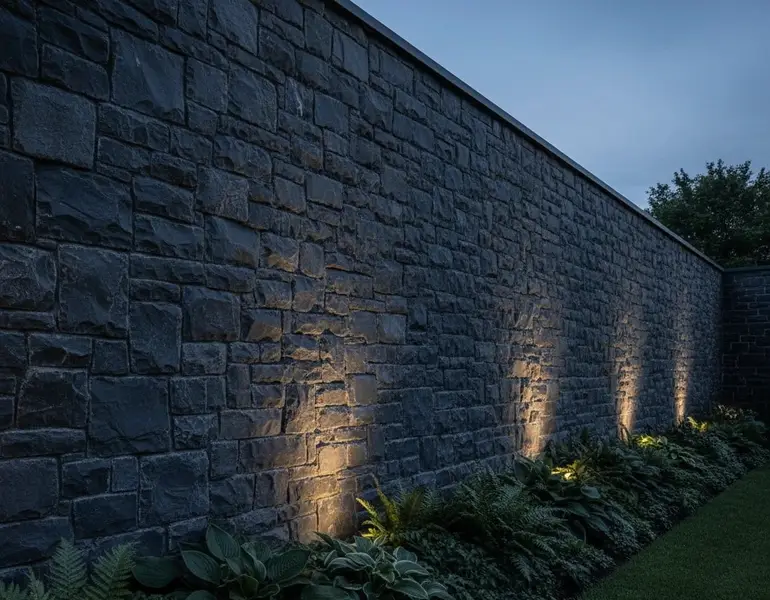 دیوار بلند محوطه با سنگ مالون نامنظم (لاشهای) در طیف خاکستری–ذغالی تیره، اجرا شده به صورت خشکهچین منظمتر