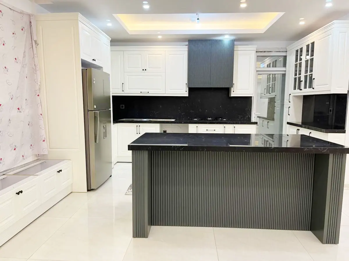 کابینت نئوکلاسیک سفید با جزیره و کاور هود خاکستری با طراحی شیاردار و میلهای